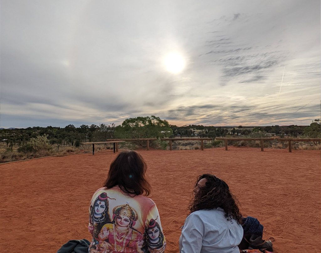 Back view of Senka and Christina against red earth and rainbow around the sun. They were spraying the skies that day